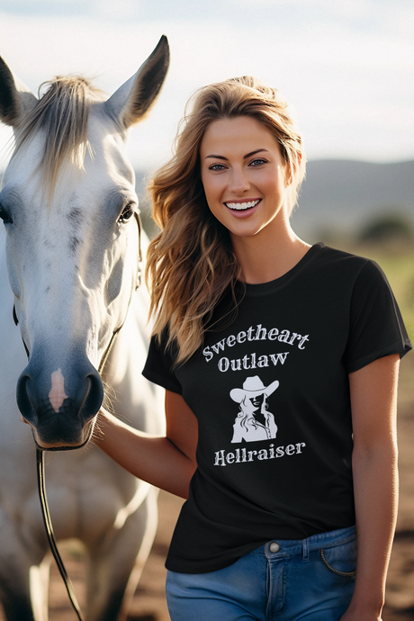 Woman wearing a black t-shirt with a graphic and text, standing next to a horse in an outdoor setting.