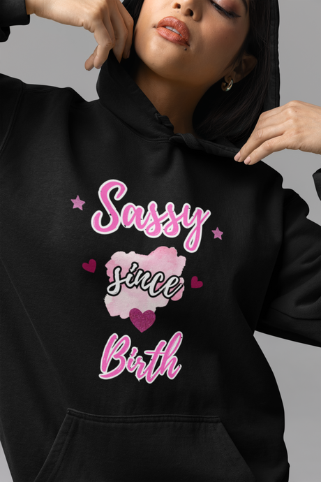 Black hoodie with 'Sassy Since Birth' text and hearts worn by a woman.